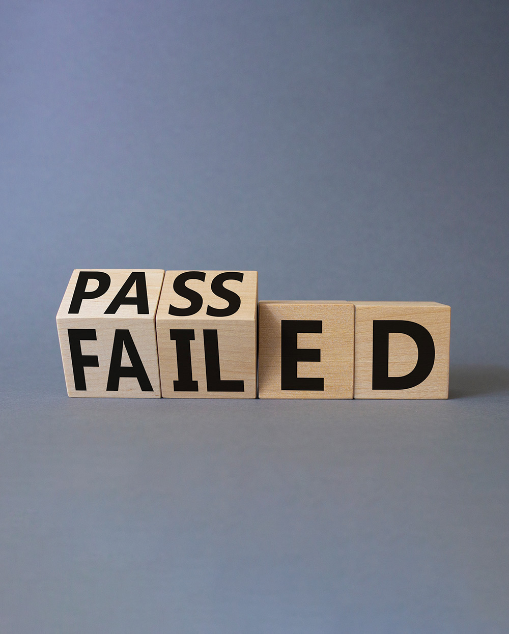 Four small wooden square blocks with first two wooden square blocks showing the word PASS facing upward on top while the word FAIL is facing downward on bottom and last two wooden square blocks showing the letters ED facing front/forward