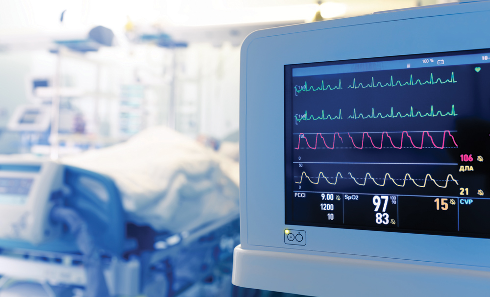 heart monitor in focus with patient in hospital bed out of focus in the background