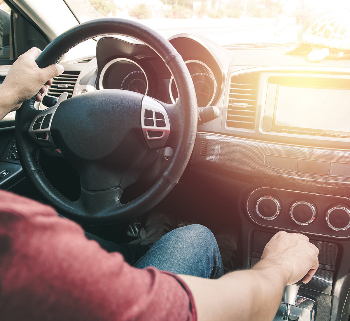 cropped view over a man shoulder as he sits in the driver seat of a vehicle, one hand rests on the steering wheel while the other rests on the gear shift