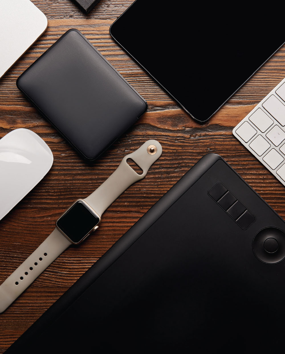 keyboard, mouse, smart watch, tablet, and charger on wood table