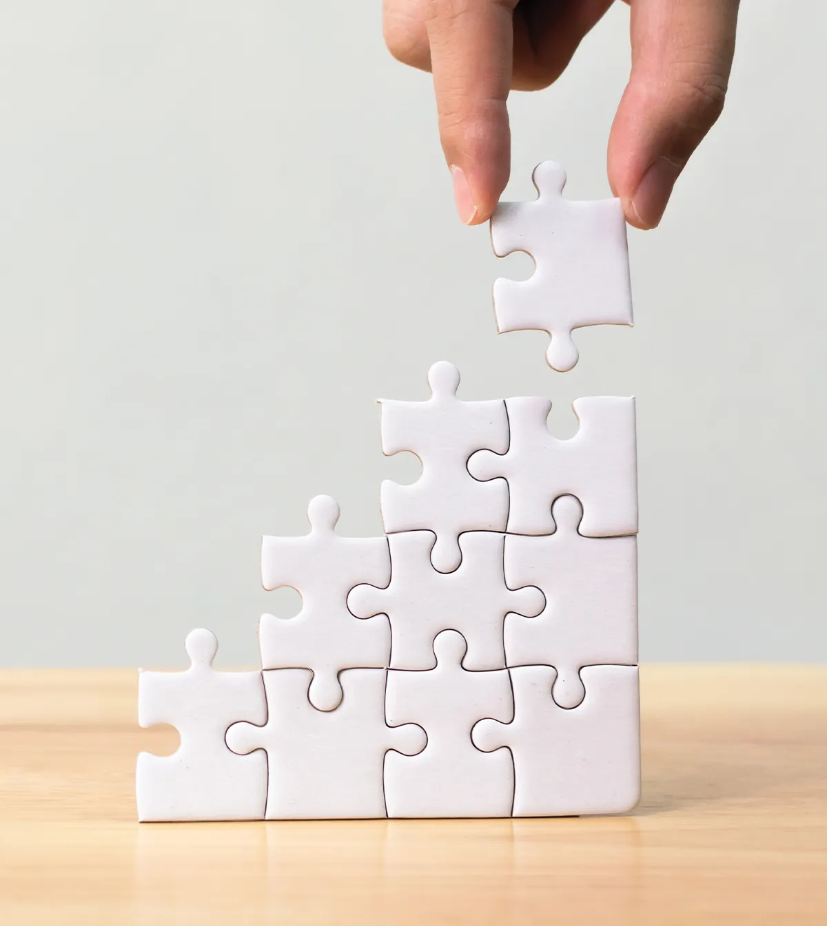A hand placing the last white puzzle piece on a stack of puzzle pieces forming a staircase or pyramid shape.