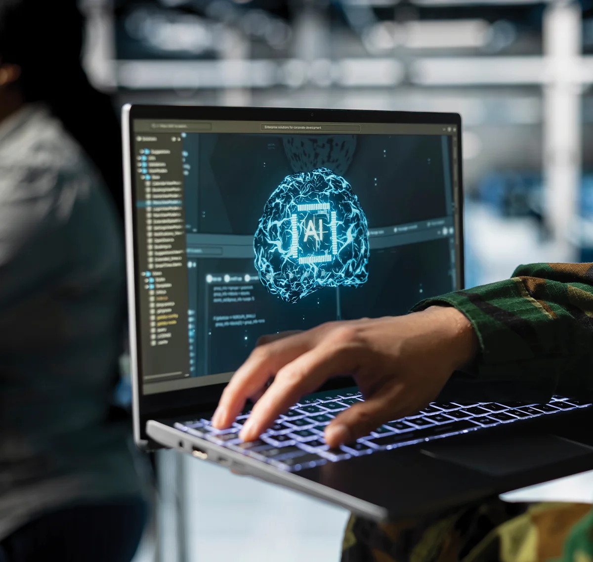 Close-up of a person in military camouflage using a laptop featuring a glowing blue digital brain and 'AI' circuit graphic on the screen.