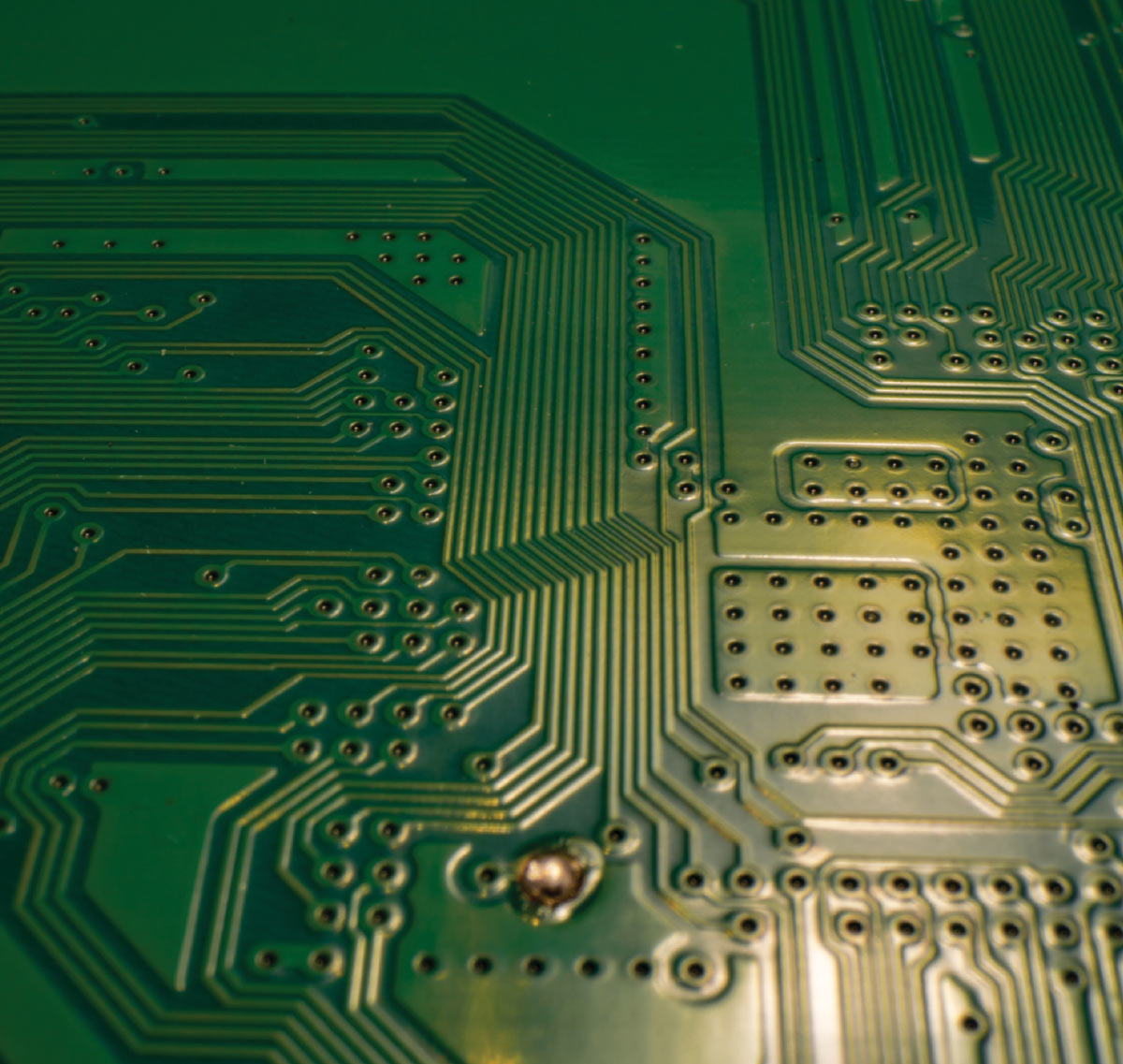 Macro view of a green printed circuit board (PCB) showing intricate copper trace patterns and solder points.