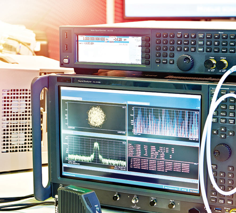 Close-up of professional test equipment, including a signal generator and a signal analyzer displaying complex waveforms, frequency spectrums, and data constellations.