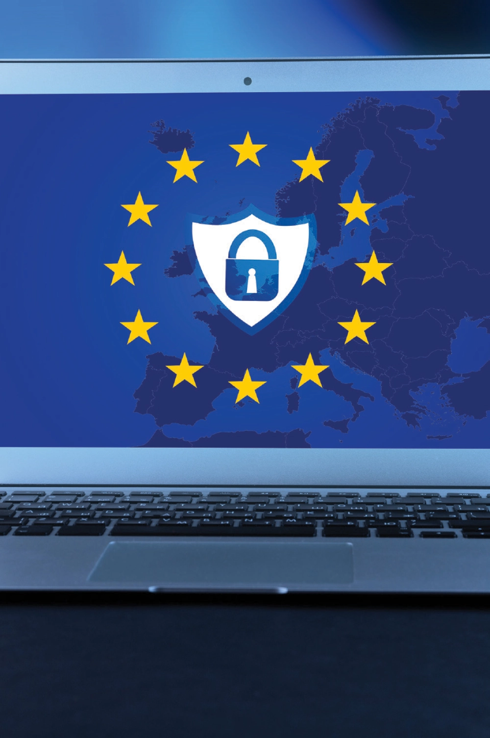 Cropped close-up digital image view of a laptop computer displayed on a surface, with the screen showing the European Union flag featuring a shield icon with a padlock in the center, representing data security and GDPR