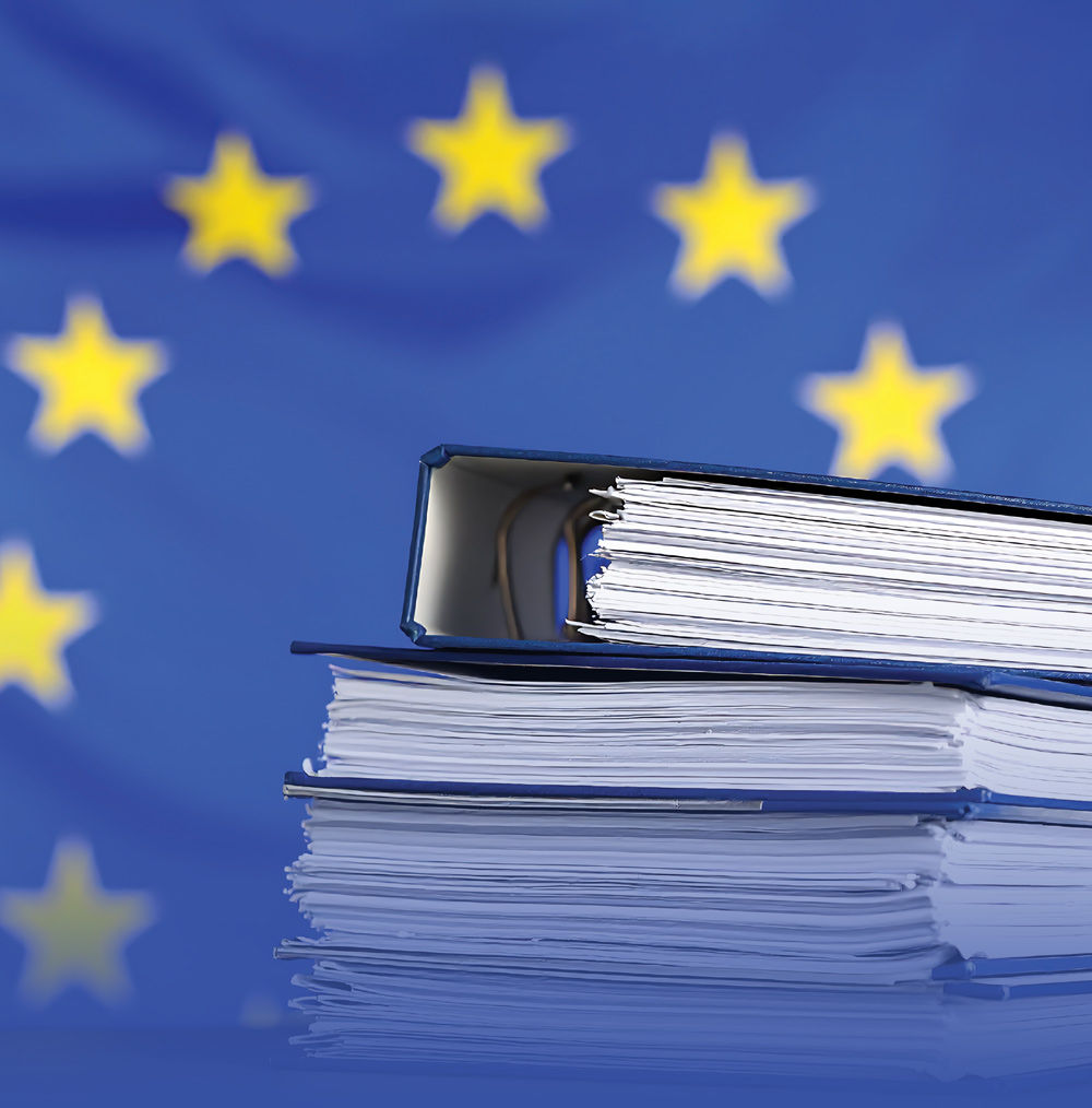 A stack of dark blue binders filled with documents against a blurred European Union flag background featuring yellow stars.