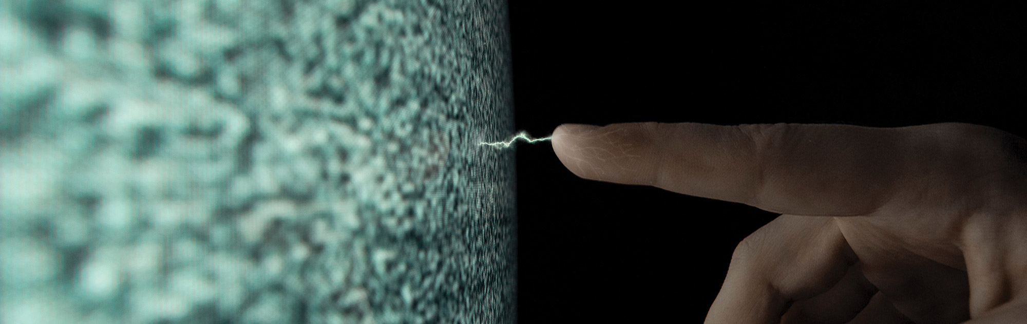 A close-up of a visible spark of static electricity arcing between a person's outstretched fingertip and a glowing television screen displaying static noise.