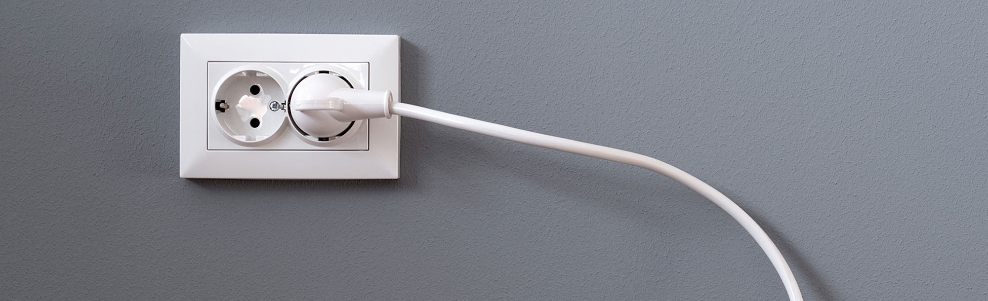 close view of a power cord plugged into an outlet on a grey wall