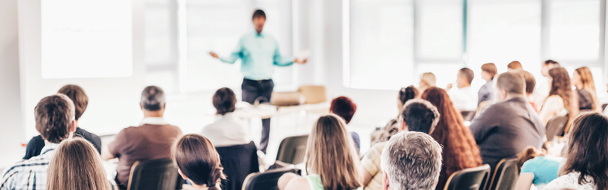 Rear view of an audience listening to a speaker presenting at a conference or seminar.