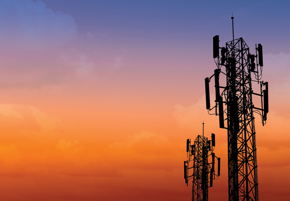 Silhouettes of two cell phone towers against a colorful orange and purple sunset sky.