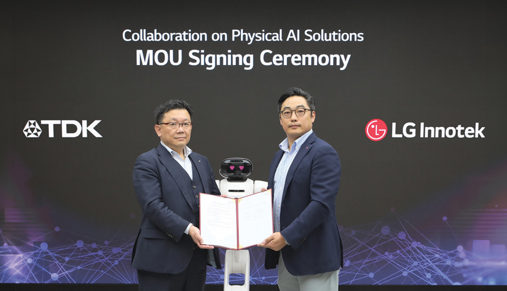 Two men in suits holding an MOU agreement document with a small robot standing between them.