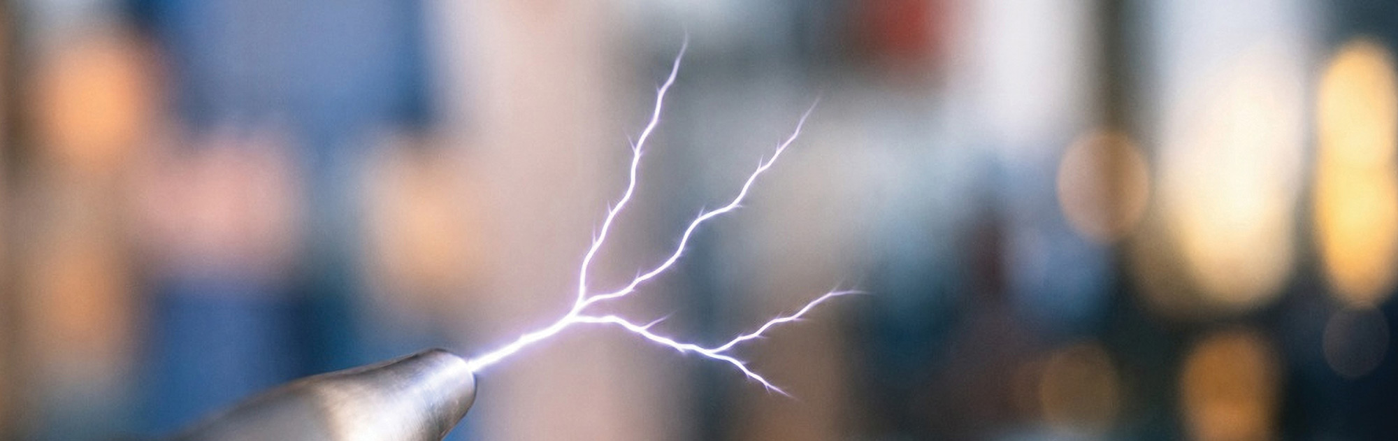 Close-up of a bright, branching electrostatic discharge (ESD) spark emitting from the tip of a metal probe against a blurred background.
