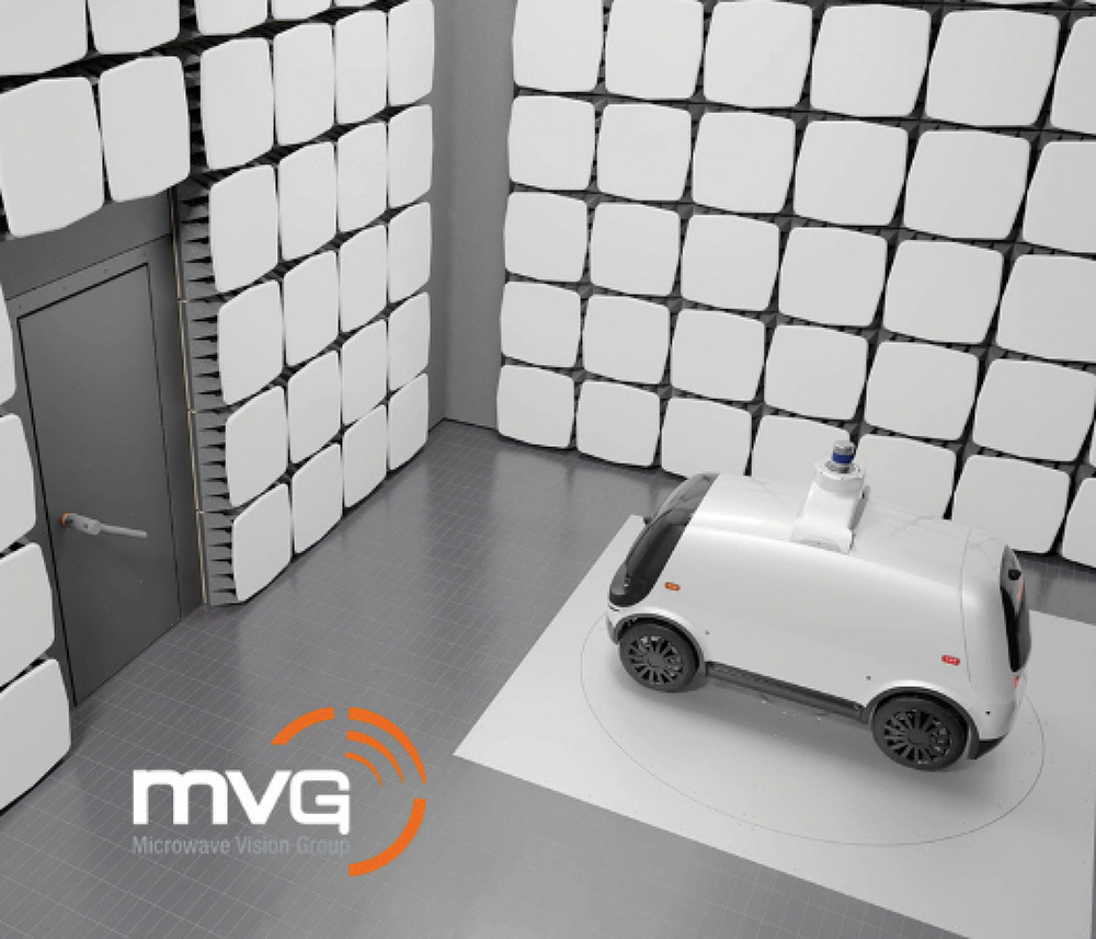 Autonomous white vehicle on a turntable inside a panel-lined Microwave Vision Group test chamber.
